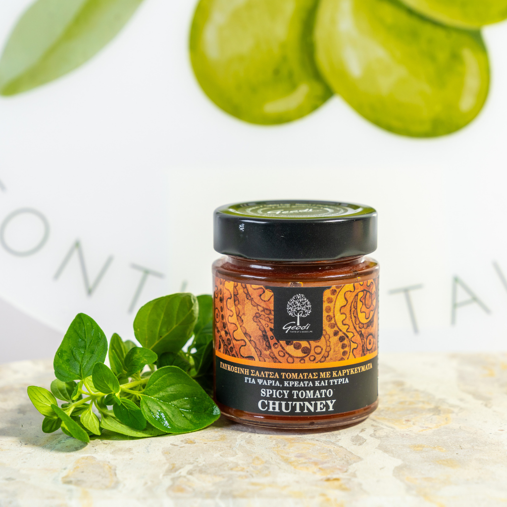 Jar of spicy tomato chutney with green leaves on a light background