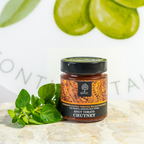 Jar of spicy tomato chutney with green leaves on a light background