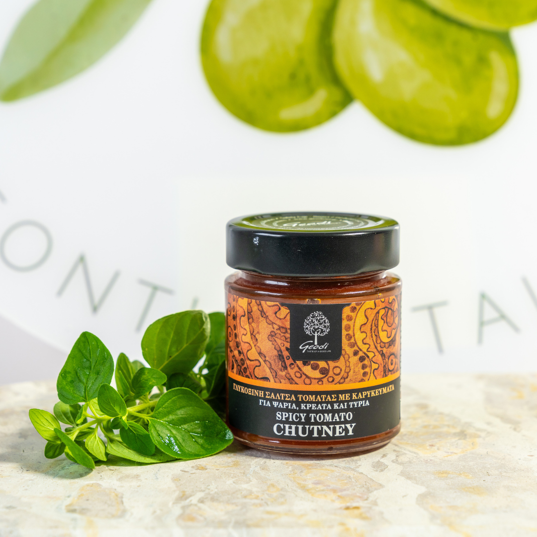 Jar of spicy tomato chutney with green leaves on a light background