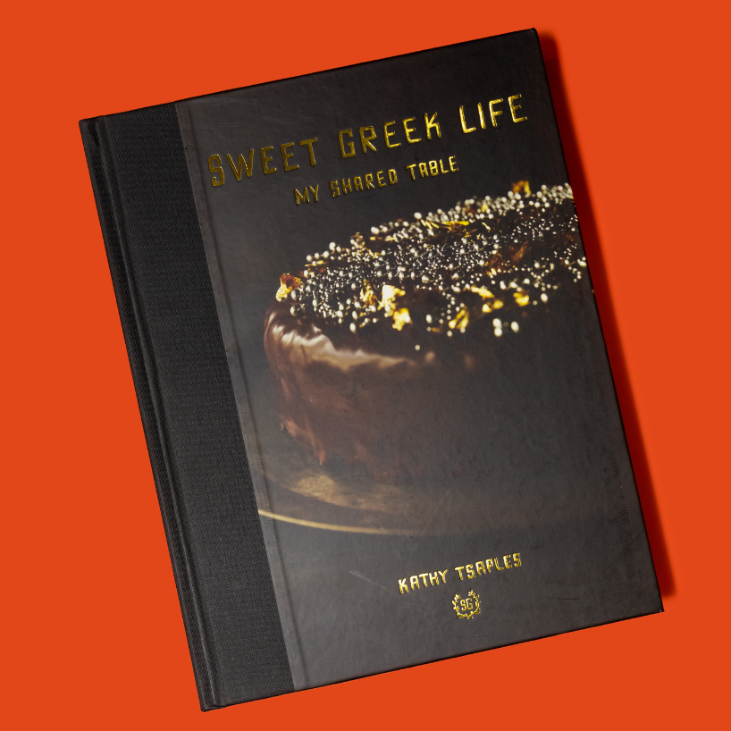 Book titled 'Sweet Greek Life: My Shared Table' with a cake illustration on an orange background