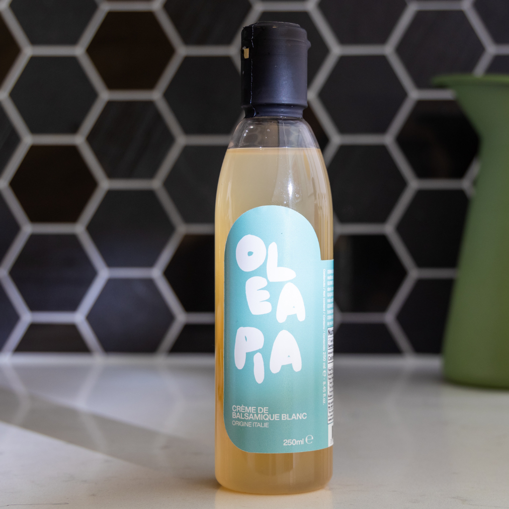 Bottle of Oleapia white balsamic vinegar on a kitchen counter with a hexagonal tile backsplash.