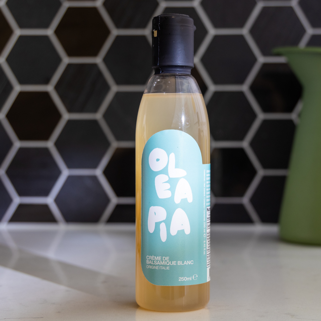 Bottle of Oleapia white balsamic vinegar on a kitchen counter with a hexagonal tile backsplash.